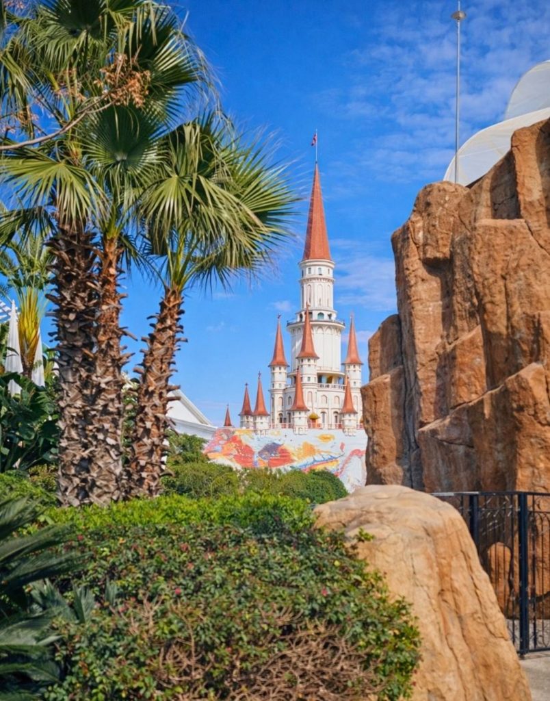 Land of Legends castle towers seen through palm trees and rock formations
