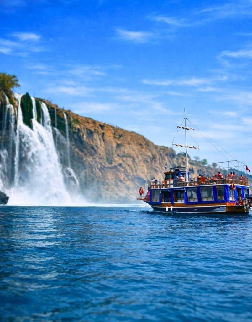 Tour boat next to massive Duden Waterfall on Antalya coast during Waterfall Boat Trip