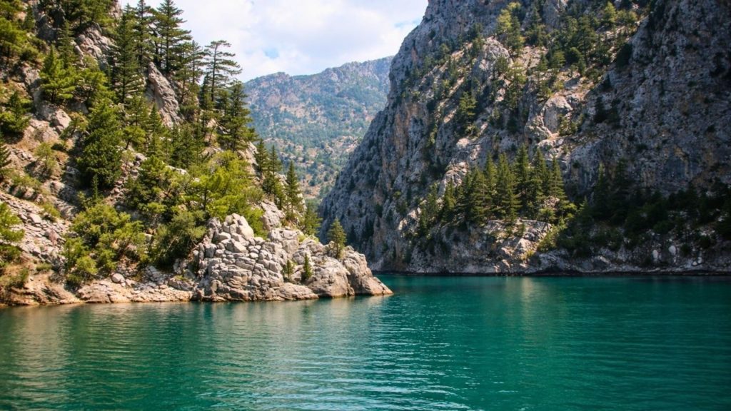 Pine covered rocky cliffs and turquoise water at Green Canyon Oymapinar lake