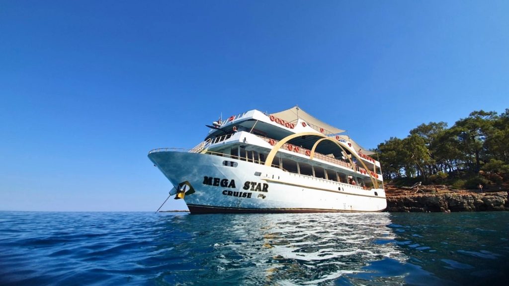 Mega Star Cruise boat close up anchored near rocky pine covered coastline Kemer