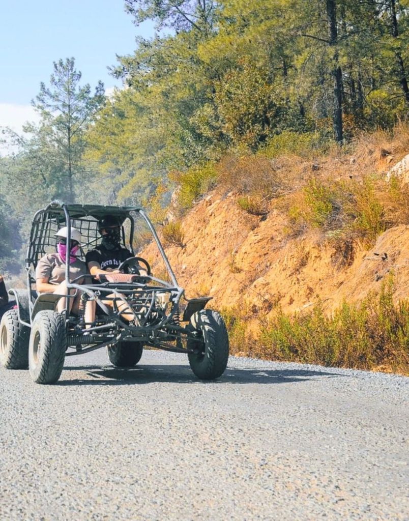 Buggy driving on mountain road with pine trees and rocky hillside in Alanya