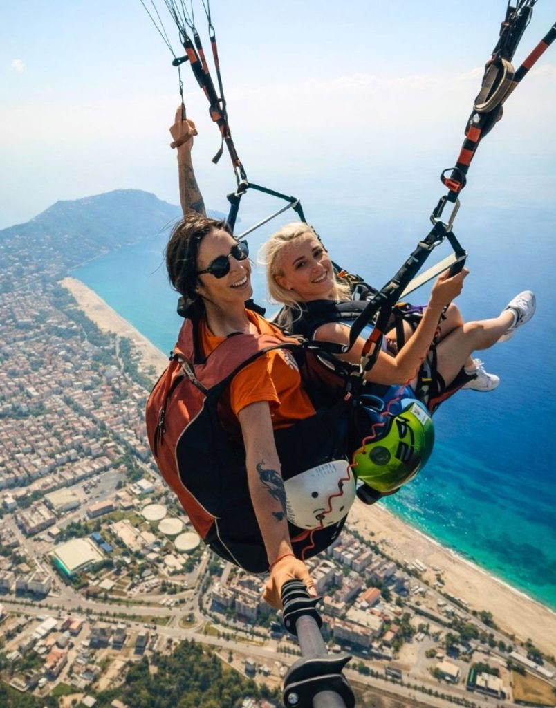 Two friends enjoying tandem paragliding flight together over Alanya coastline
