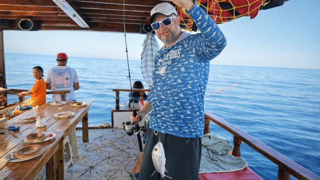 Happy visitor showing his catch on the Alanya fishing boat with family dining
