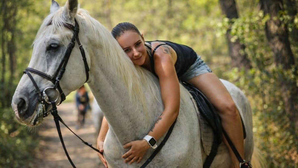 Woman hugging white horse on forest trail during Alanya horse safari