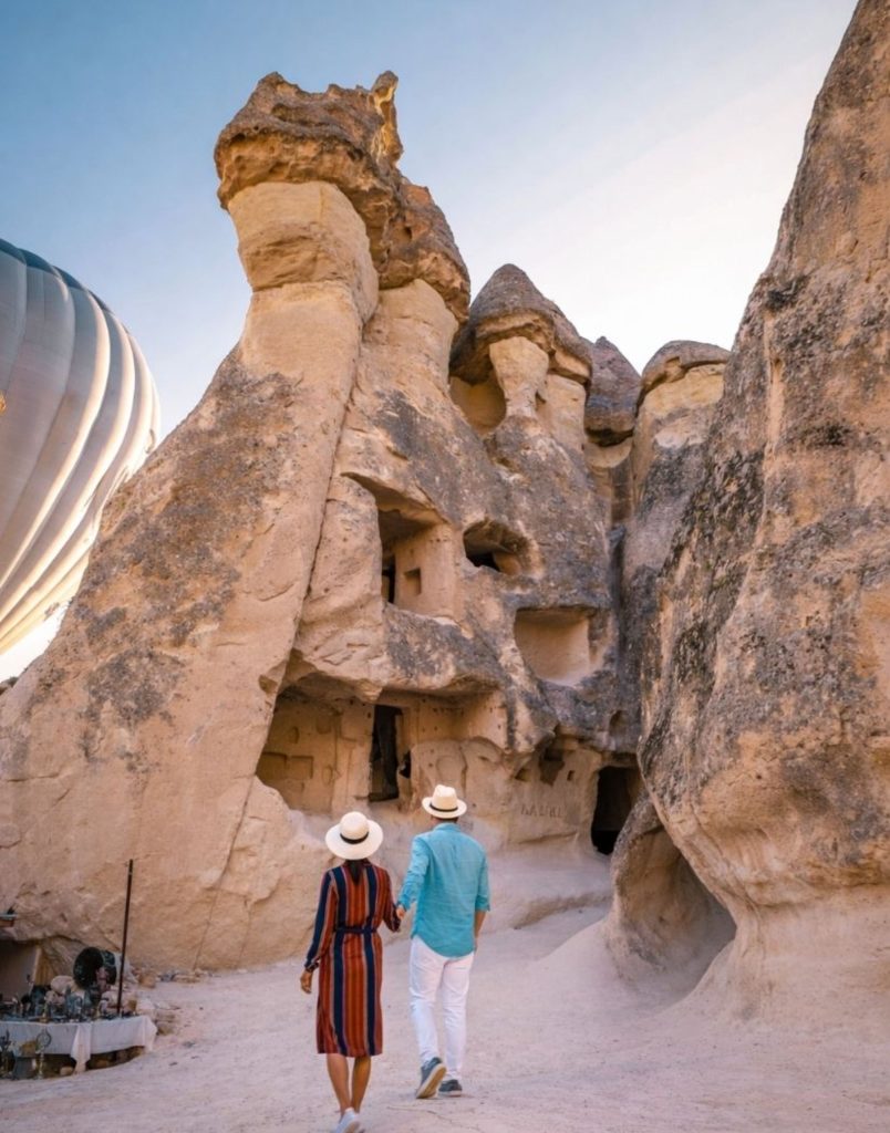 Couple walking towards Cappadocia fairy chimneys with hot air balloon in background