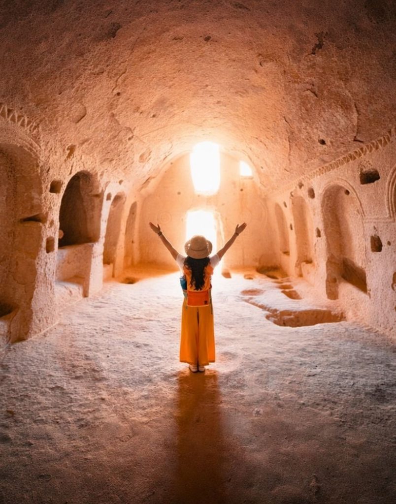 Traveller inside ancient underground cave church with golden light in Cappadocia