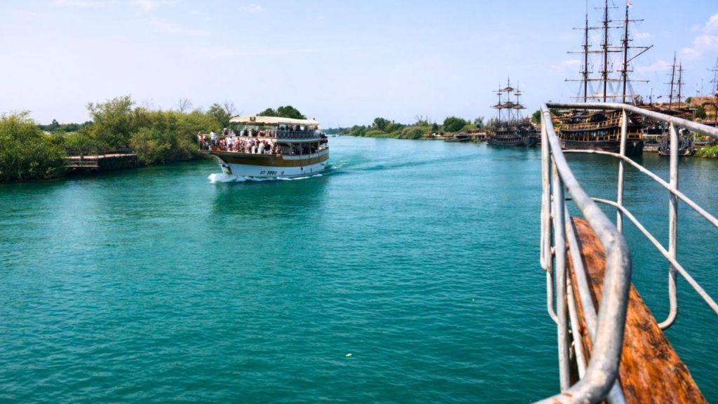 Tour boat leaving Manavgat River harbour with pirate ships docked turquoise water