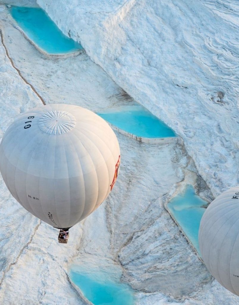 Hot air balloons flying directly above Pamukkale white travertine terraces with turquoise thermal pools
