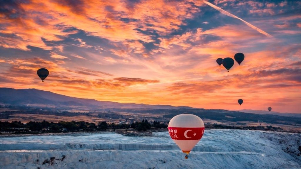 Hot air balloons flying over white Pamukkale travertines at sunset with dramatic orange sky