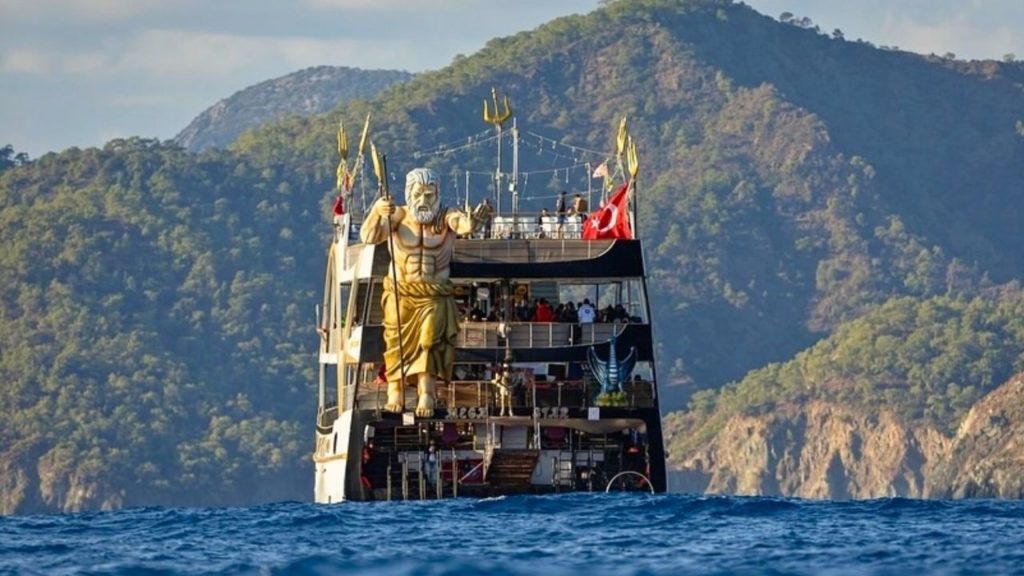 Iconic Mega Star party boat with giant Poseidon statue cruising along Antalya mountains