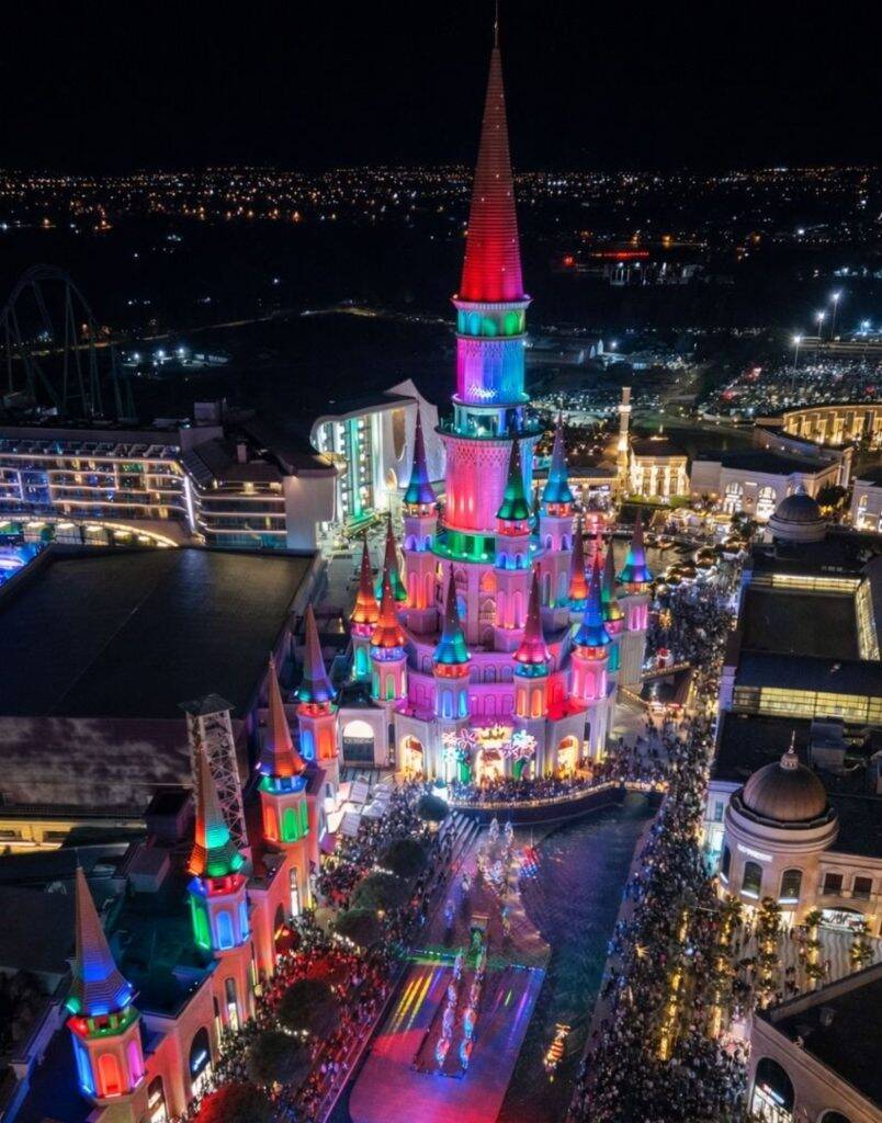 Aerial night view of Land of Legends castle lit up in rainbow colors during night show Antalya