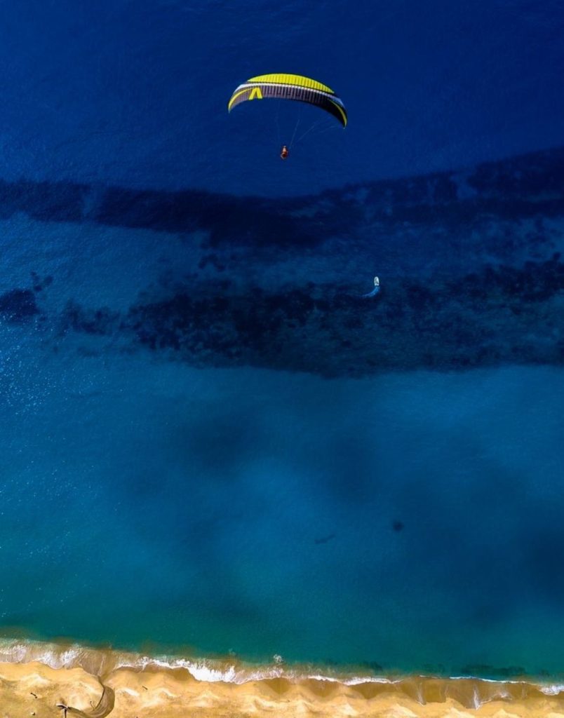 Aerial drone view of paraglider flying over deep blue Mediterranean sea and golden Antalya beach