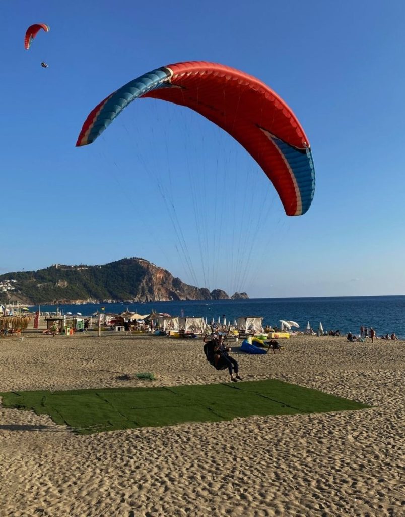 Paraglider landing on Antalya beach with castle hill and sea in background