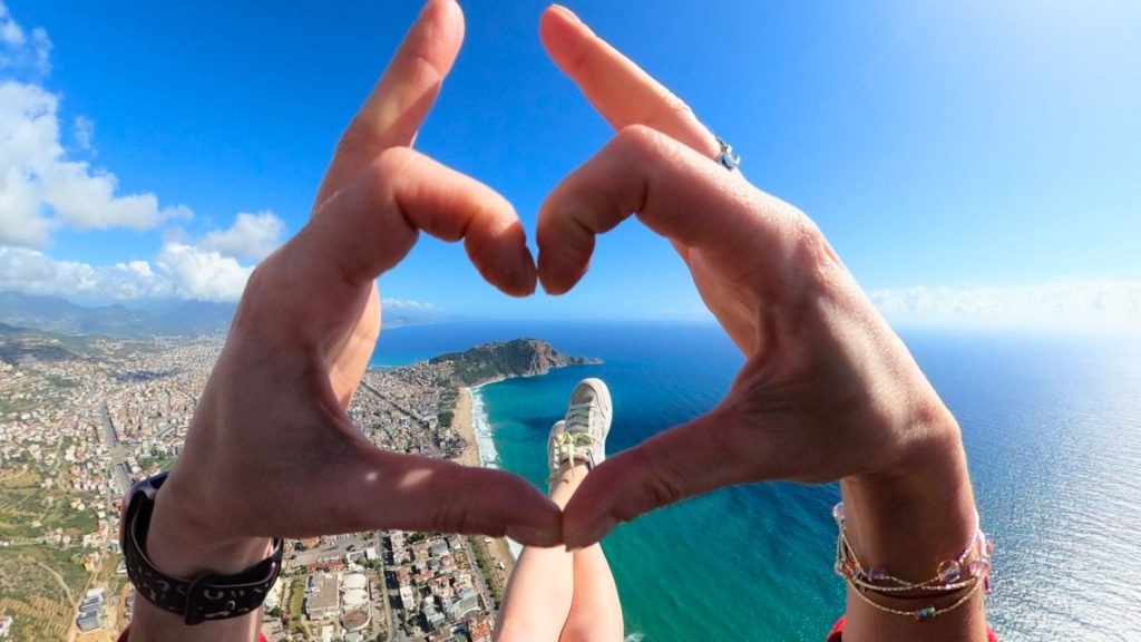 Heart-shaped hands during paragliding flight over Antalya coast and turquoise sea