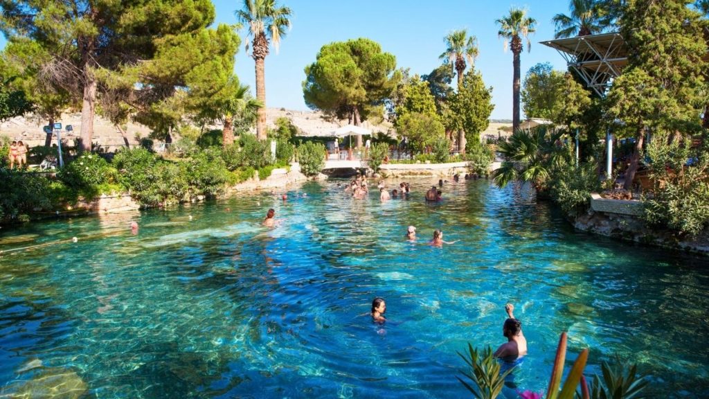 Visitors swimming in Cleopatra Antique Pool surrounded by palm trees on a Pamukkale tour from Antalya