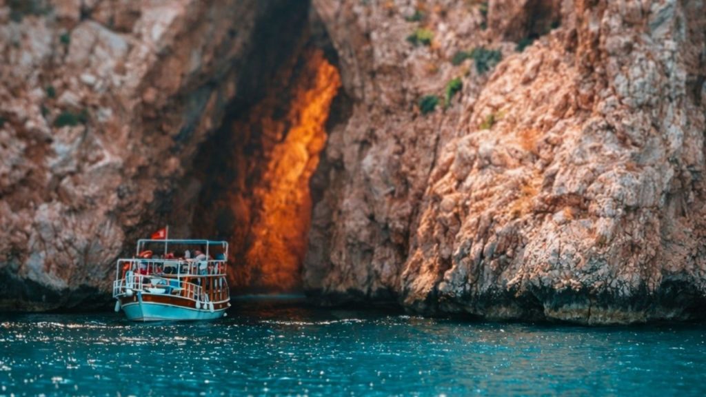 Tour boat at dramatic sea cave with golden light near Suluada Island during boat trip from Antalya