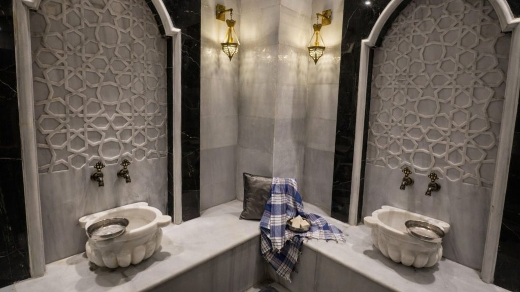 Elegant marble washing corner with Ottoman geometric wall patterns and golden lamps inside Alanya hammam