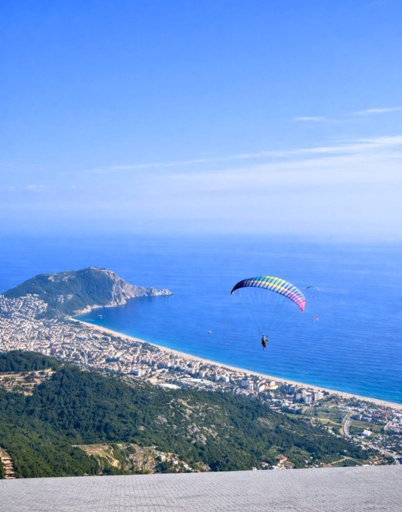 Colourful paraglider flying over Alanya with Cleopatra Beach and castle hill panorama