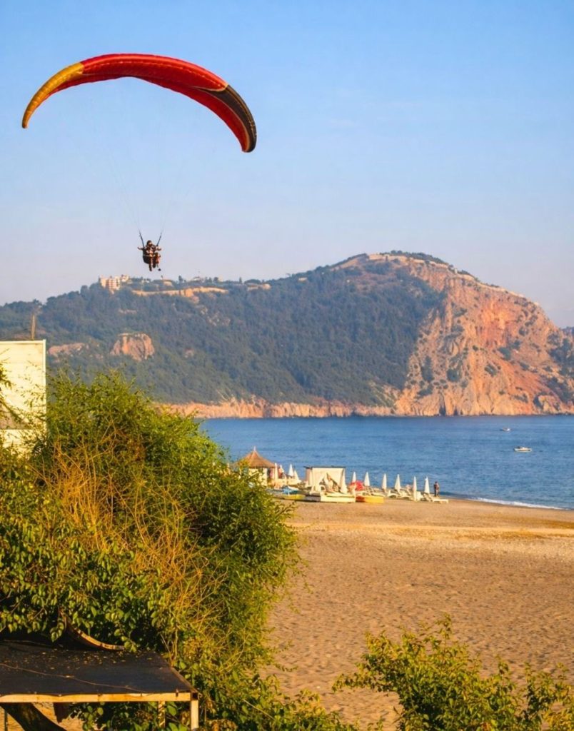 Paraglider landing on Alanya beach with castle hill and sea in background