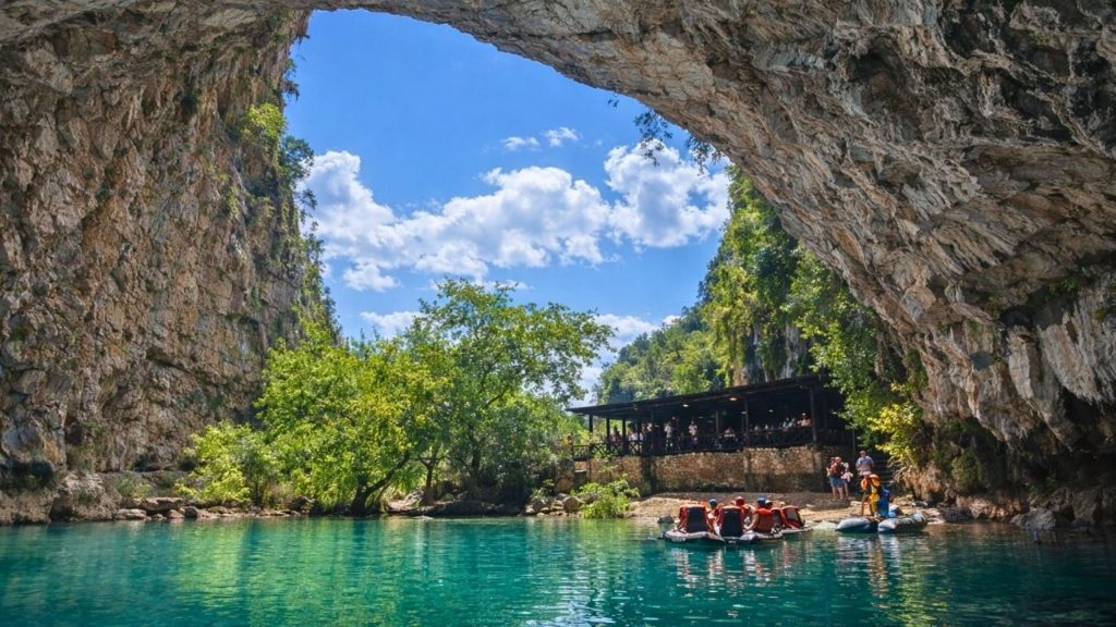 side altinbesik cave tour entrance with natural rock arch turquoise lake and inflatable boats