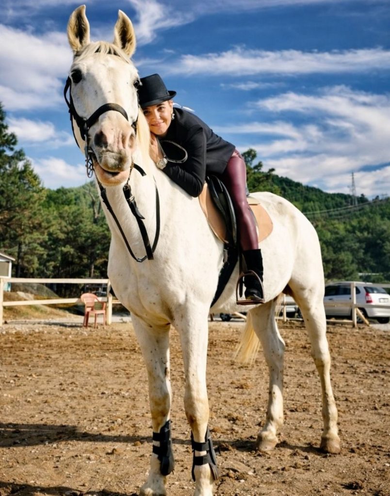 white arabian horse at side horse riding ranch with green forested hills
