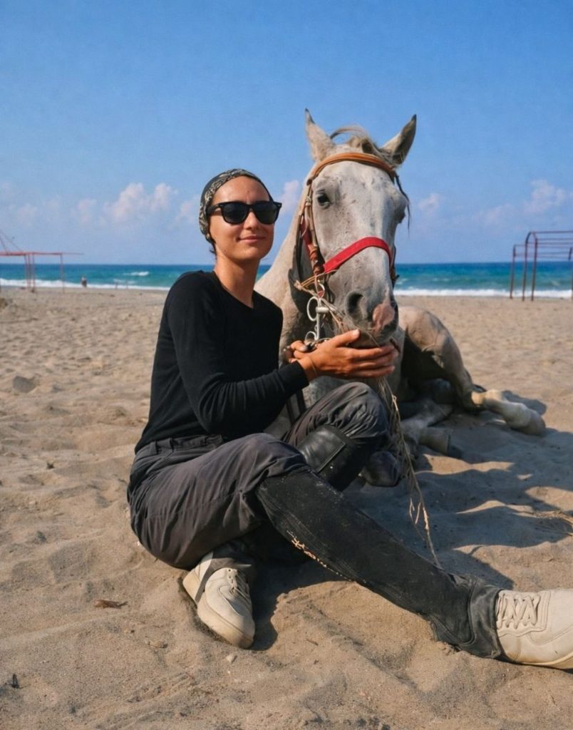 grey horse resting on sandy beach with mediterranean sea during side horse riding tour