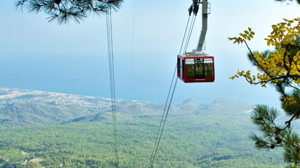 Olympos Cable Car gliding over green pine forest with Antalya coast below