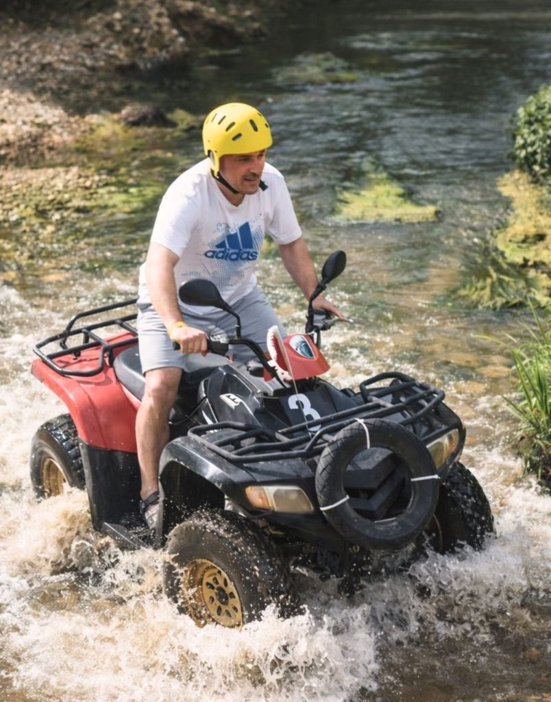 belek quad biking through a river with water splashing around the wheels
