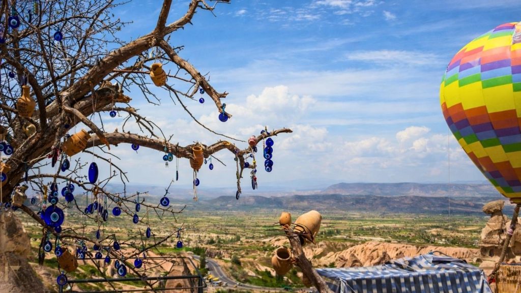 Evil eye tree with pottery and colourful hot air balloon over Cappadocia valley panorama