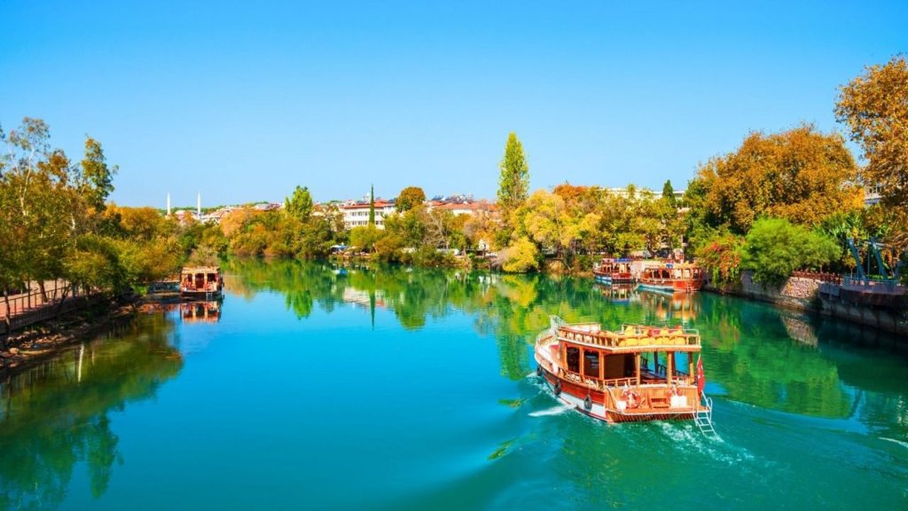 Traditional wooden boat on crystal-clear Manavgat River with colorful tree reflections