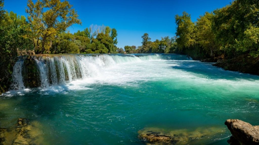 Manavgat Waterfall with turquoise water flowing over rocks surrounded by green trees