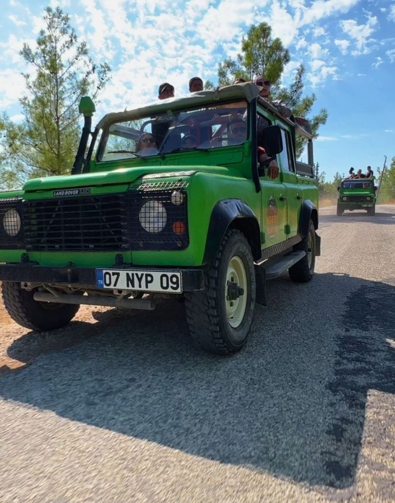 Belek jeep safari green Land Rover close up on road with convoy behind pine forest