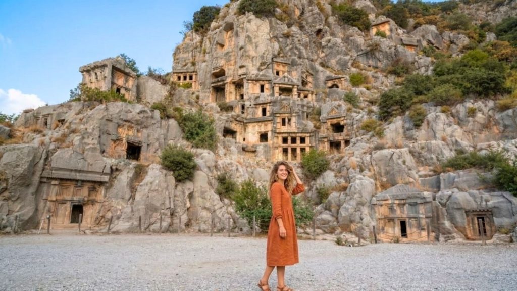 Visitor in front of famous Lycian rock tombs carved into mountainside at Myra on Demre Myra Kekova tour from Alanya