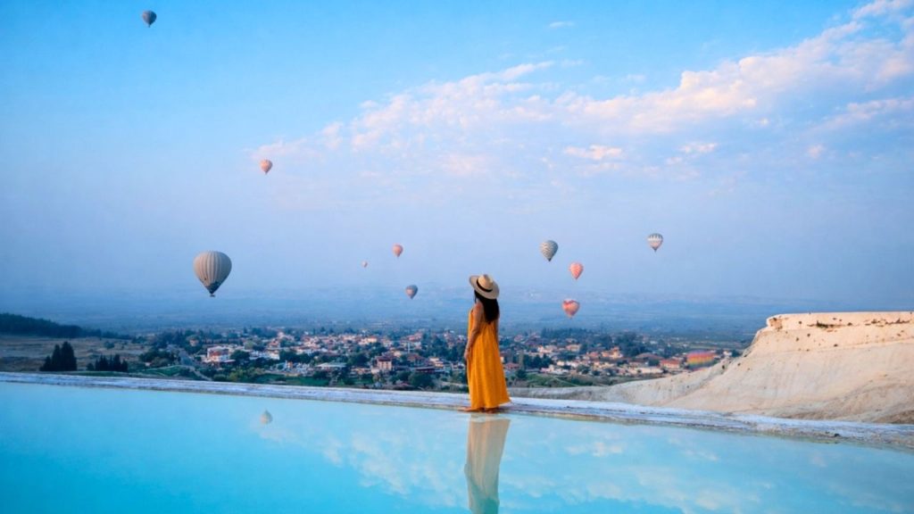 Pamukkale thermal pool with hot air balloons floating in the blue sky above the white travertines