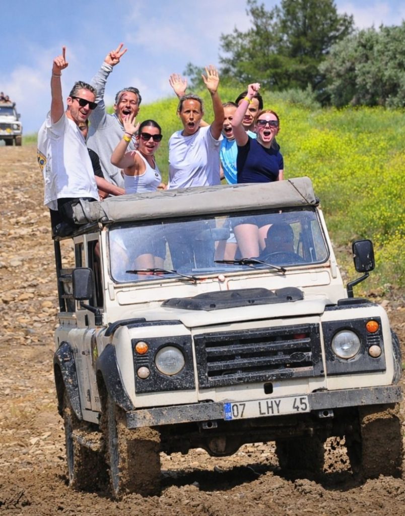 Antalya jeep safari on muddy off-road trail with group hands up and green countryside