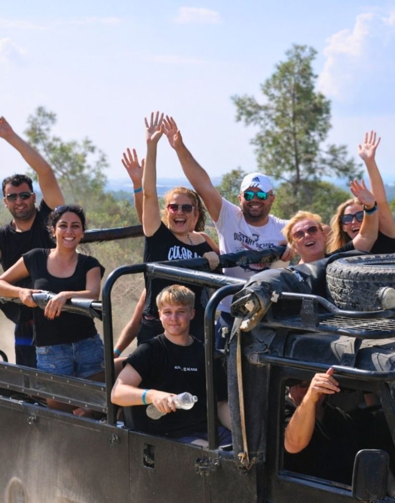 Group of happy tourists with arms raised in an open-top jeep during Antalya safari tour