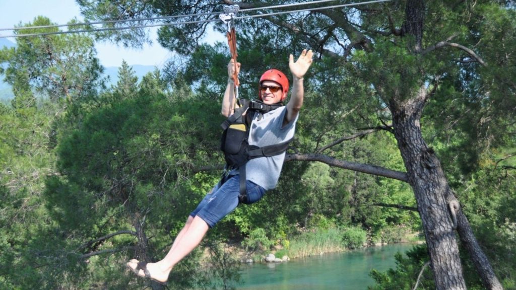 Tourist on a zipline flying over turquoise river and pine forest in Antalya